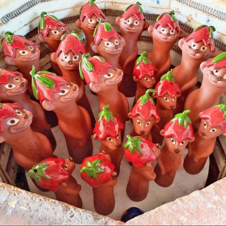 Erdmännchen Eine Gruppe von Tontöpfen mit Gesicht und Erdbeerhut in einem kreisförmigen Arrangement.
