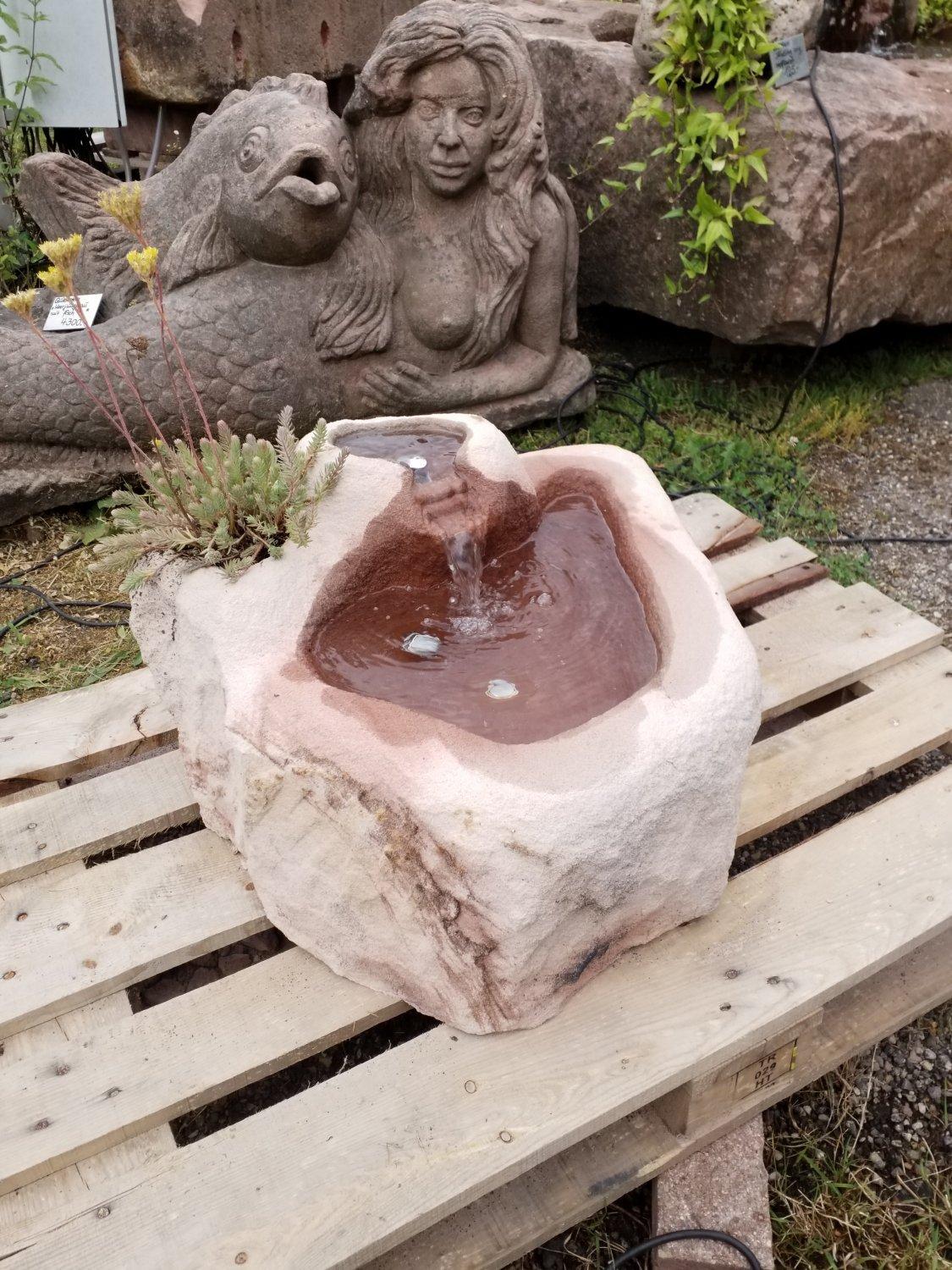 Brunnen aus Stein in Herzform mit fließendem Wasser und Pflanzen dekoriert.