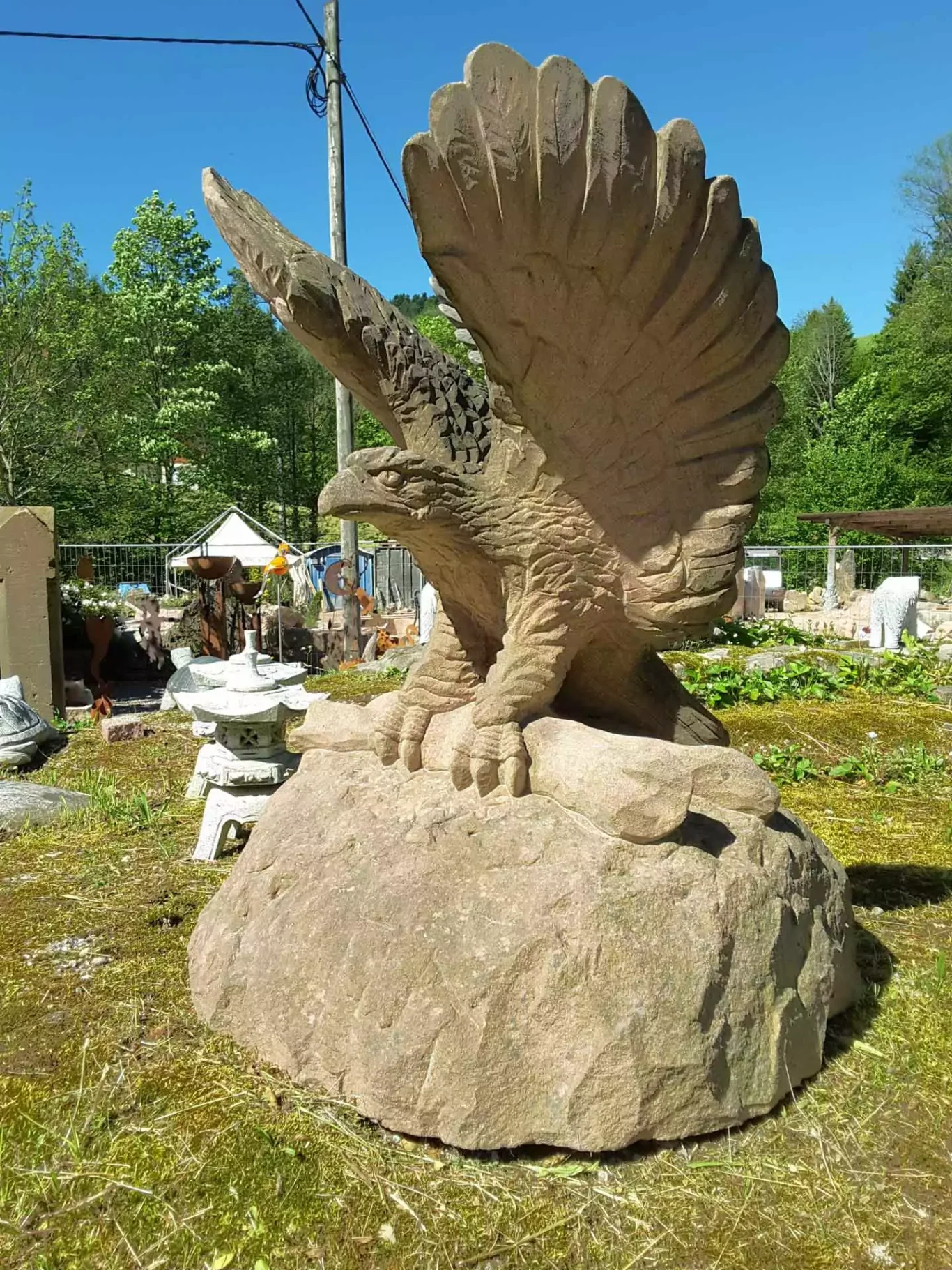 Steinskulptur eines Greifvogels auf einem Felsen in einem Garten.
